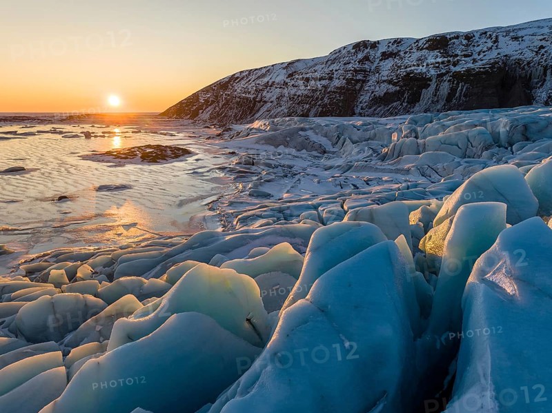 Captivating sunrise in Skaftafell, Iceland, featuring glowing icebergs with a stunning backdrop of snow-draped hills, epitomizing the serene beauty of winter