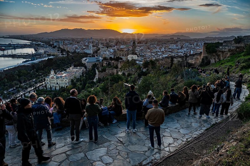 MALAGA, SPAIN - JANUARY 31, 2026: High angle view of a crowd of tourists gathered at a scenic viewpoint watching the vibrant golden sunset over Malaga city and port, Spain