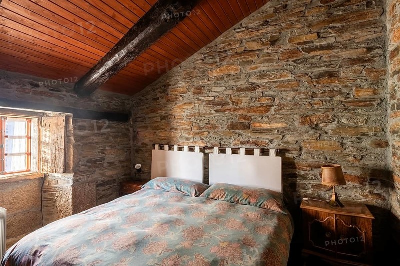 Cozy rustic bedroom featuring exposed stone walls and wooden ceiling, with charming vintage furnishings, located in a traditional country house in Lugo, Spain