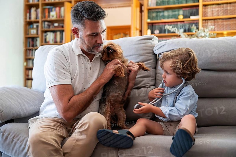 A joyful gay couple shares a playful moment with their young son and pet dog on the living room couch, embracing family, love, and togetherness in a cozy home setting