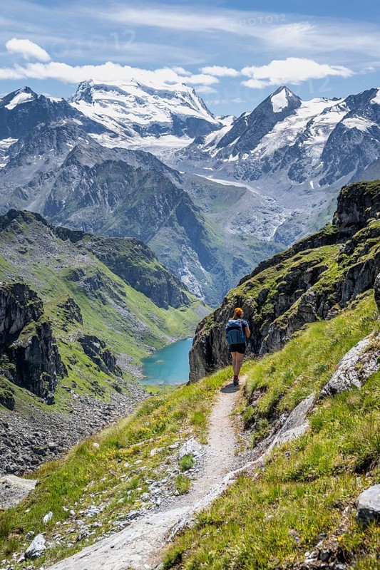 Hiker on hiking trail, mountain lake Lac de Louvie with glaciated summit of the Grand Combin, Val de Bagnes, Valais, Switzerland