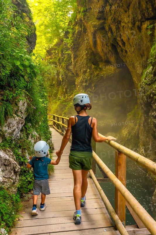 Mother and son wearing helmets, enjoying a walk through the scenic vintgar gorge in slovenia, holding hands and exploring nature together