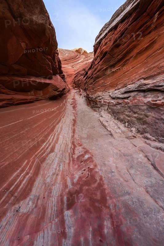 Vibrant red and orange striated sandstone walls form a narrow canyon path in White Pocket, Arizona, offering a dramatic natural spectacle typical of the southwestern United States