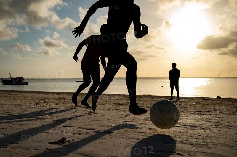 Close-up silhouette of a person running to kick a soccer ball on a tropical beach at sunset with a golden sky in Zanzibar, Tanzania