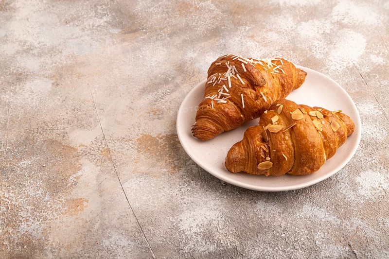 Croissant on white plate on brown concrete background, side view, copy space