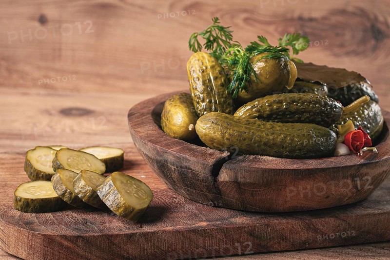 Pickled cucumbers in a wooden bowl with herbs and spices, close-up, rustic style