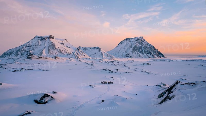A breathtaking view of snow-covered mountains in Iceland, illuminated by the soft glow of sunrise. The vast expanse of icy terrain creates a serene winter atmosphere