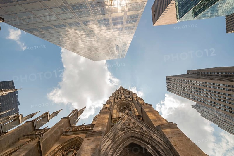 Low angle shot capturing the dynamic architecture of Manhattan with reflective skyscrapers towering over the historic St. Patrick's Cathedral