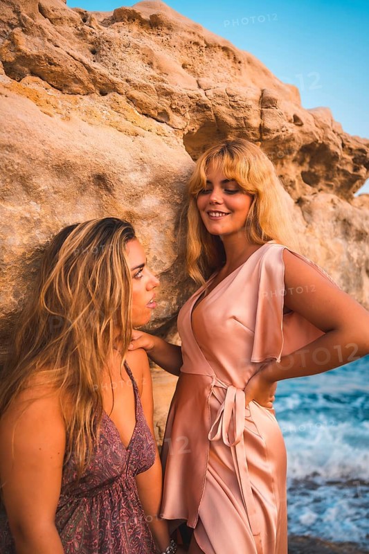 Romantic gazes of a couple of Caucasian girls with pink dresses, in a summer sunset on the beach by the sea