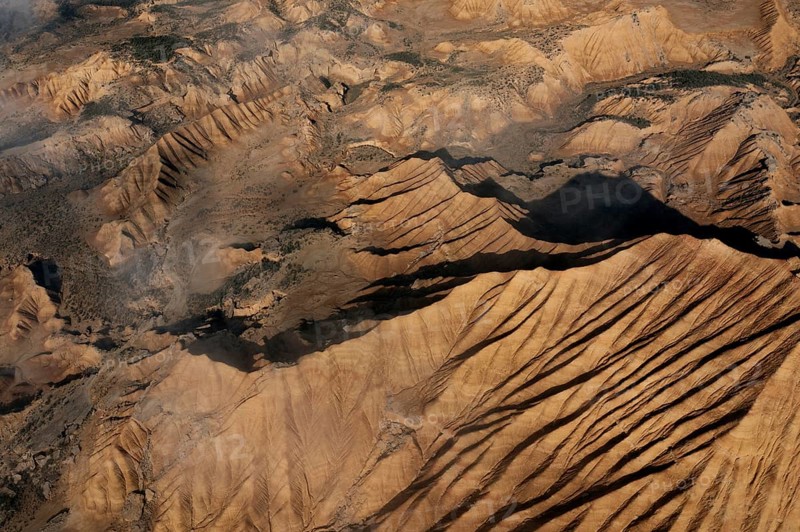 Aerial view depicting rugged desert terrain marked by dramatic ridges and gullies Sunlight casts shadows, highlighting the intricate patterns of erosion A breathtaking landscape