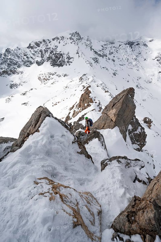 Mountaineer descending the narrow ridge of Piz Laviner, view of mountain panorama in wintry mountain landscape with dramatic clouds, Grisons Haute Route, Albula Alps, Rhaetian Alps, Grisons, Eastern Switzerland, Switzerland