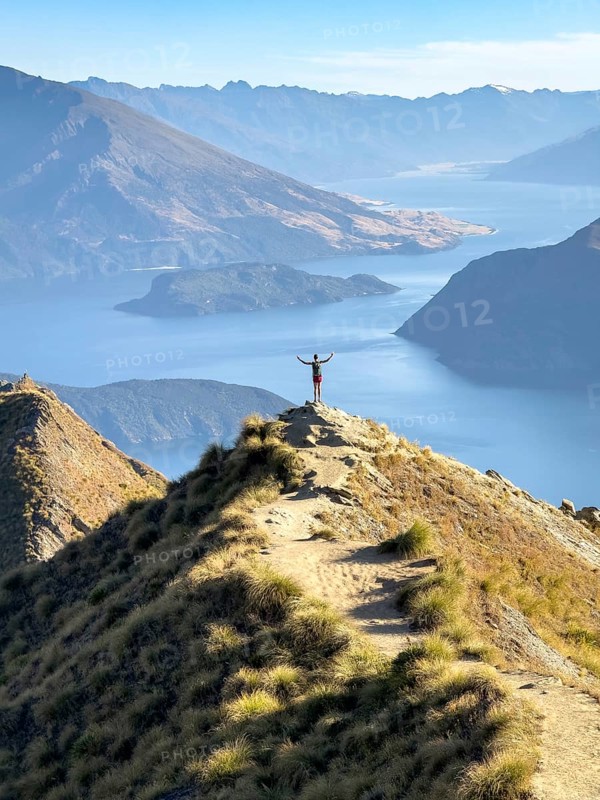 Person with outstretched arms on the hiking trail to Roys Peak Lookout, Lake Wanaka, Wanaka, South Island, New Zealand, Oceania