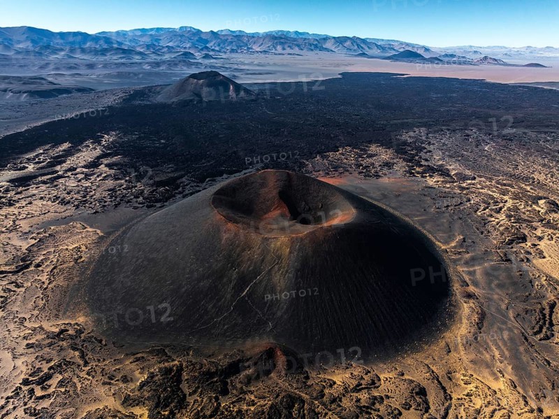 A mesmerizing aerial view captures the Antofagasta Volcano in Catamarca, Argentina, showcasing its majestic form and rugged terrain set against a backdrop of distant mountains