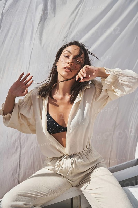 A stylish woman enjoys a sunny day on a rooftop She is wearing a polka-dot bikini top and a loose linen outfit, capturing the essence of a relaxed summer lifestyle