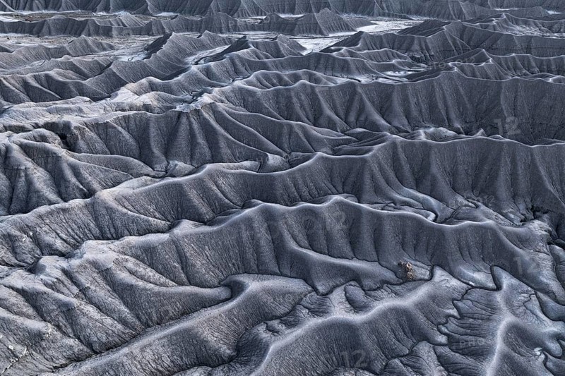 Expansive aerial view showcasing the unique and textured gray terrain of Caineville Mesa near Hanksville, Utah, with intricate erosion patterns highlighted under overcast skies