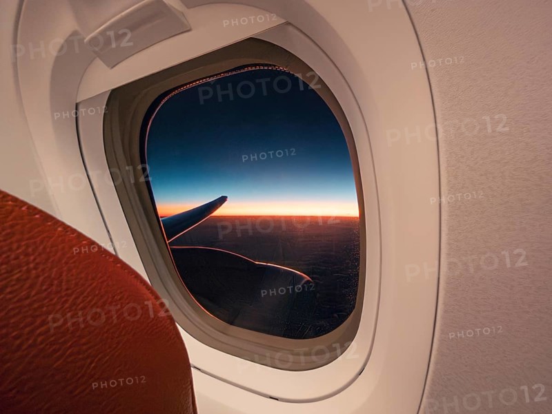 A panoramic view of a vivid sunset and aircraft wing, seen through the porthole of an airplane, capturing the beauty of aerial travel