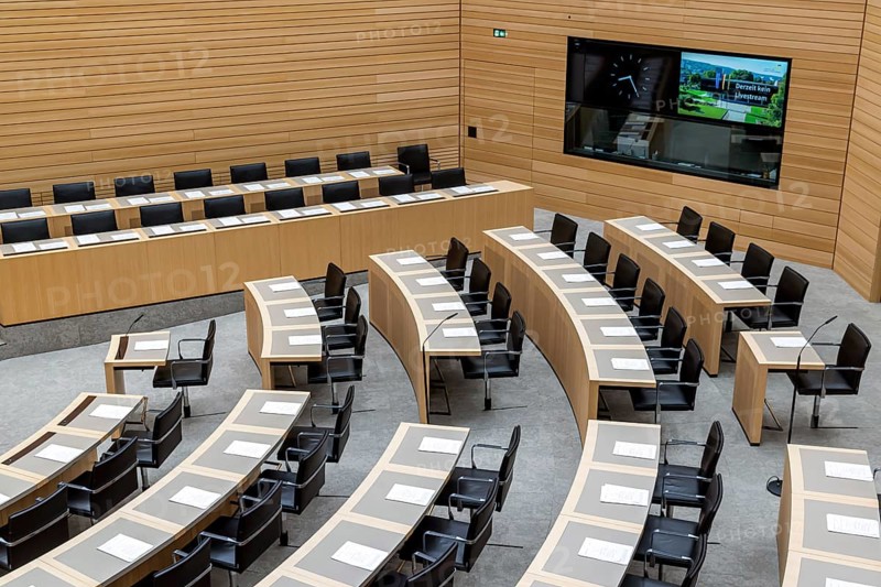 Plenary hall deserted with the seats of deputies and the government bank. Behind it is the coat of arms of the federal state. The state parliament of Baden-Württemberg is the state parliament based in Stuttgart, Baden-Württemberg, Germany