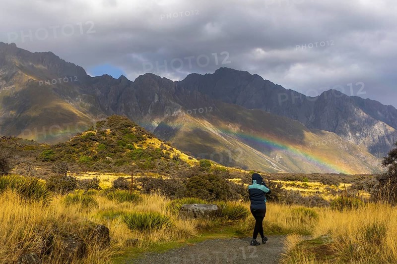 A woman in a winter coat explores the breathtaking autumn landscape of Mount Cook, New Zealand. Golden grasses and rugged terrain create a stunning natural panorama