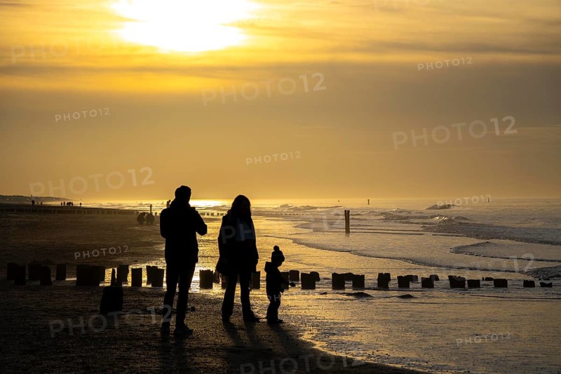 Winter on the North Sea, sunset at sea, beach walkers, coastal protection, through wooden posts, paalhoofden, on the beach, breakwater, the piles rammed into the sandy soil in double rows slow down the waves and ocean currents and thus slow down the flow rate of seawater, so less sand is washed away from the standing position, near Domburg, Walcheren peninsula in the Dutch province of Zeeland