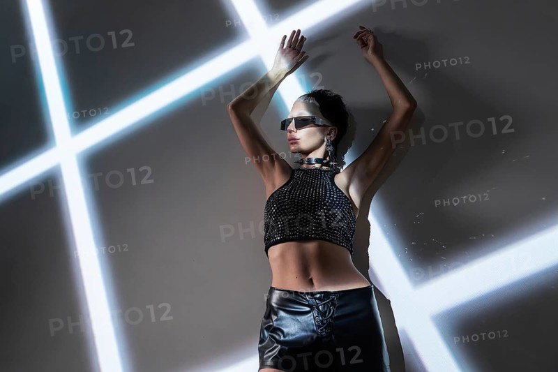 A stylish woman models futuristic cyberpunk attire against a backdrop of intersecting neon lights. The high-tech ambiance exudes a sleek, modern aesthetic inspired by sci-fi culture