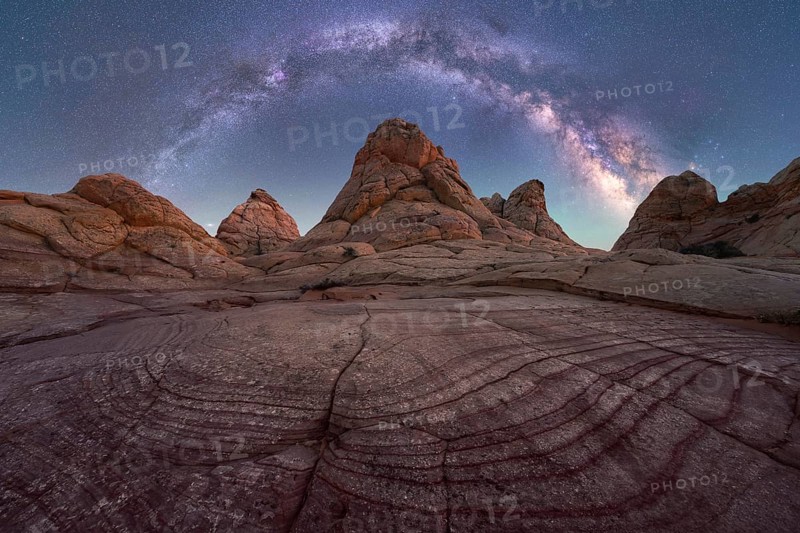 A stunning capture of the Milky Way arching across a clear night sky over unique rock formations in a desert landscape, showcasing the beauty of nature and the cosmos in Coyote Buttes, Arizona