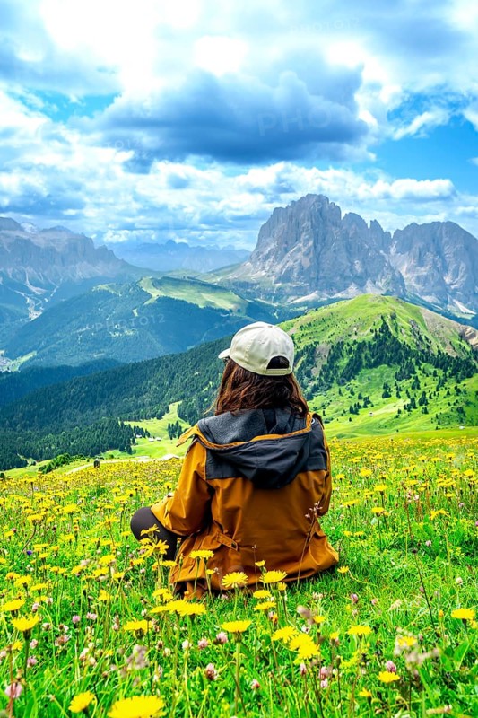 Hiker relaxing in a meadow of yellow flowers admiring the odle mountains in the italian dolomites