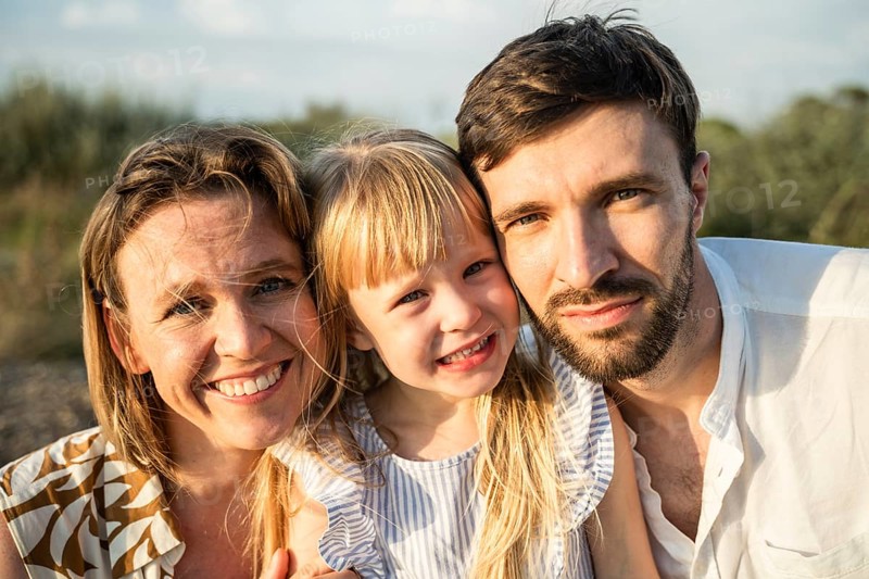 A joyful family of three enjoying a sunny day at the beach in Italy, capturing precious moments and smiles, showcasing love and togetherness in a natural, sandy setting