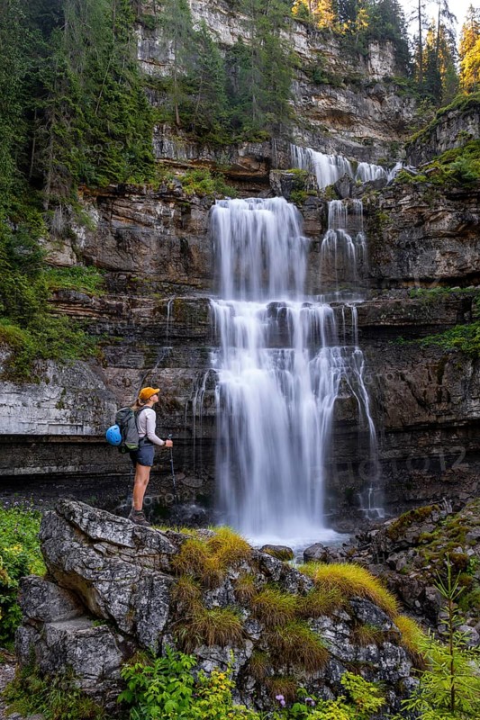 Young pretty hiker standing on rocks in front of Cascata di Mezzo waterfall, long exposure, Vallesinella, Brenta, Trentino, Italy