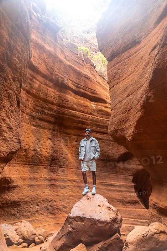 Tourist standing on a rock, admiring the breathtaking view of barranco de las vacas canyon in gran canaria, spain, during a sunny day