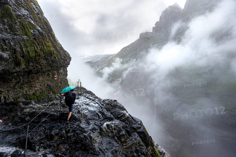 Hikers on a rocky hiking trail Clouds covered in mystical rock gorge with waterfalls, hike to Berghaus Bäregg, Bernese Alps, Bernese Oberland, Switzerland