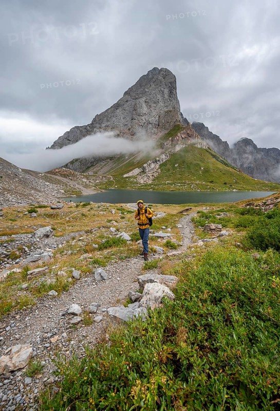 Mountaineers on a hiking trail with a view of rocky cloudy mountains and Wolayersee, hiking trail to Wolayerseehütte, cloudy mountain peaks, Carnic Alps, Carnic High Trail, Carinthia, Austria