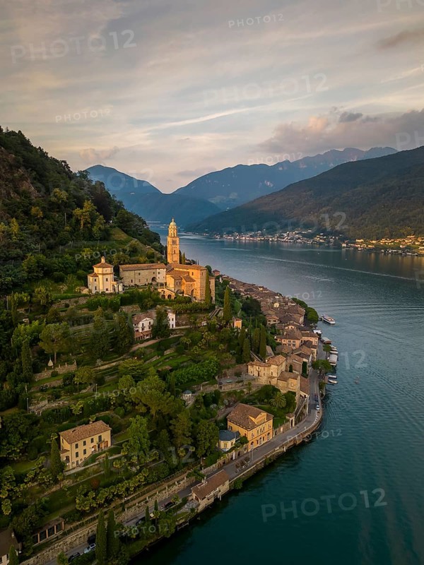 Stunning aerial view of Morcote village in Lugano, Switzerland, showcasing historic architecture surrounded by lush greenery and the serene waters of Lake Lugano at sunset