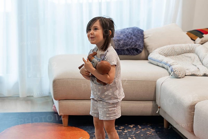 A young girl joyfully embraces her doll in a cozy living room, symbolizing love and innocence. The child's playful expression adds warmth to the vibrant home setting