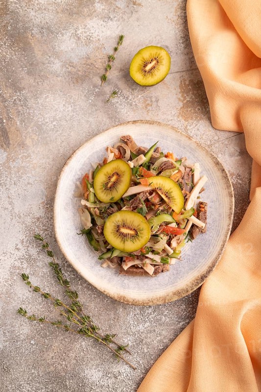Meat salad with beef kiwi and vegetables on brown concrete background and orange linen textile. top view, flat lay, close up