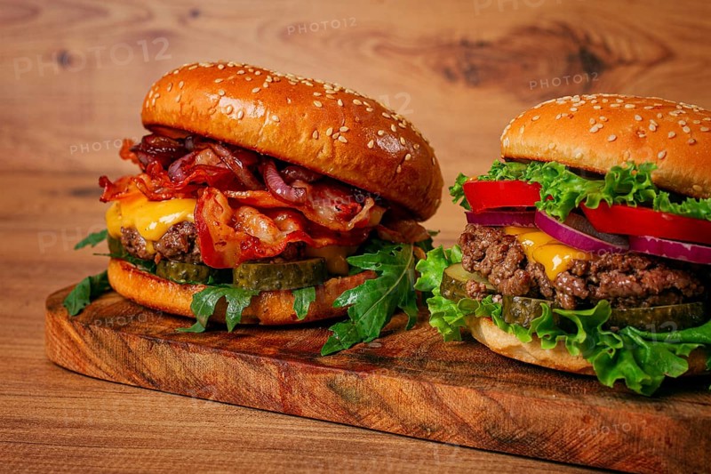 Two burgers with beef patty, fried bacon, cheddar cheese, tomatoes, homemade, no people