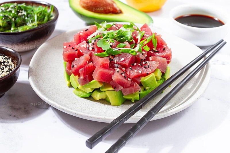 Fresh tuna tartare with avocado served on a marble table with soy sauce and seaweed salad