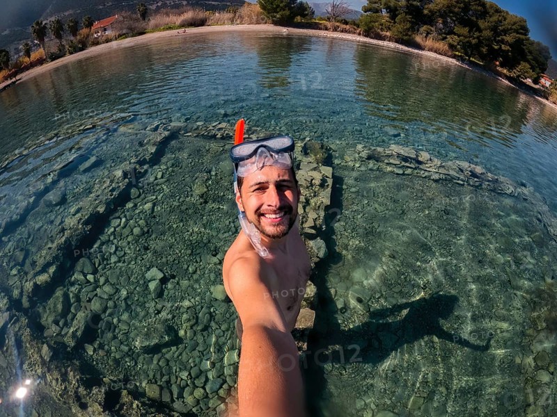 A snorkeler captures a selfie in the crystal-clear waters of Greece. The serene setting highlights the vibrant underwater life and the joy of aquatic exploration in a beautiful environment