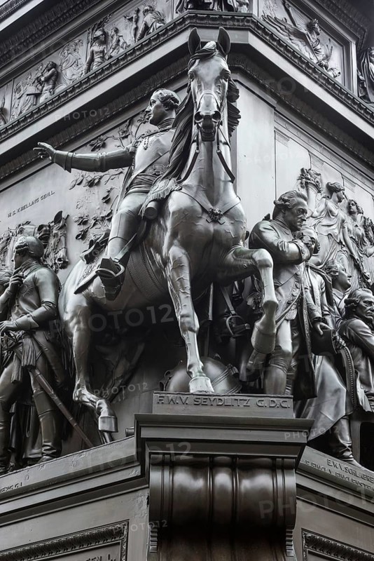 Historical equestrian statue of Frederick the Great at the Forum Fridericianum from 1839-1851, cavalry general Friedrich Wilhelm Freiherr von Seydlitz-Kurzbach in uniform on a horse with fearful eyes and open mouth, artist: Christian Daniel Rauch, Berlin School of Sculpture, transition from classicism to realism, bronze, bronze sculpture, pedestal, portrait, imposing, equestrian monument, equestrian statue, sculpture, detailed historical depiction, Berlin Mitte, City of Berlin, Germany