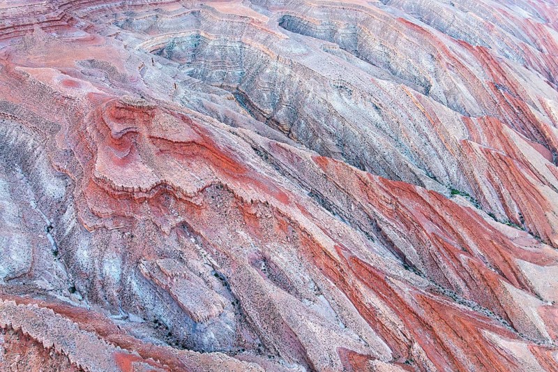 Striking aerial view featuring the vivid, layered rock formations of a canyon near the San Juan River in Utah, showcasing a natural palette of reds, oranges, and browns