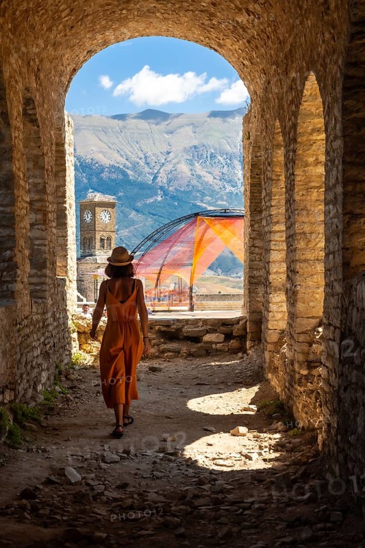 A woman walking in the arches of the fortress of the Ottoman castle of Gjirokaster or Gjirokastra and in the background the church with the clock tower. Albania, Kulla e Sahatit
