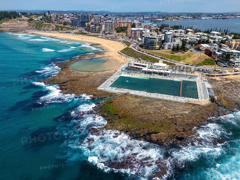 Aerial view of a picturesque coastal pool and neighboring beach in New South Wales, Australia, showcasing vibrant turquoise waters, rocky landscapes, and urban skyline