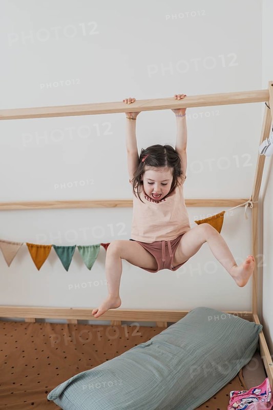 A joyful young girl hangs and plays indoors, showcasing her energetic spirit. The room is colorful and welcoming, reflecting a happy family environment filled with love and laughter