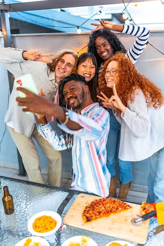 Vertical photo of a smiling african man taking selfie with multi-ethic friends in a roof party during sunset