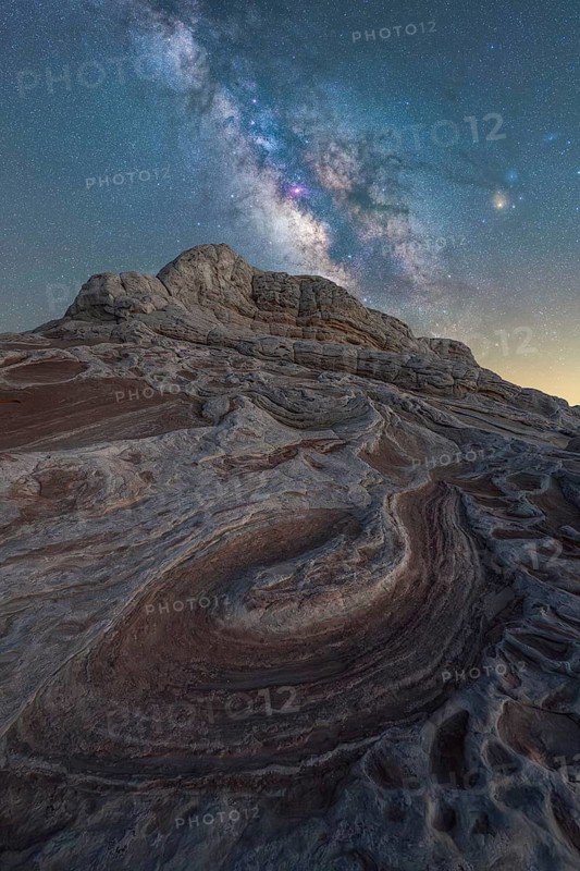 The Milky Way sparkles in a clear night sky over the dramatic and swirling sandstone formations of White Pocket, Arizona, showcasing an otherworldly desert nightscape