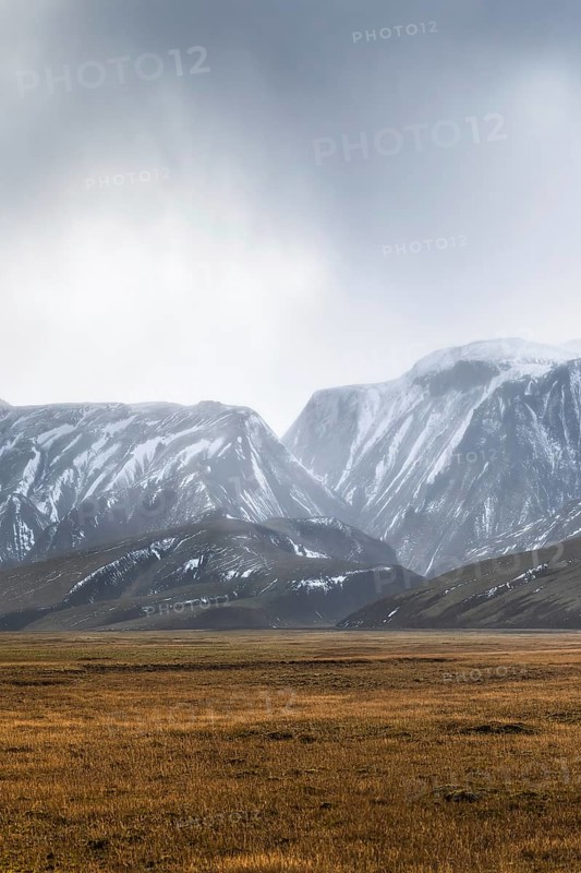 Expansive view of Iceland's highlands showcasing majestic, snow-capped mountains under a moody sky, with vast meadows stretching in the foreground