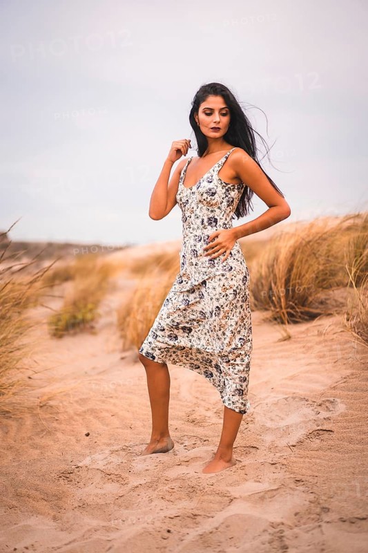 Portrait of a Caucasian brunette stroking her hair in a white flowered dress, in the sand on the beach
