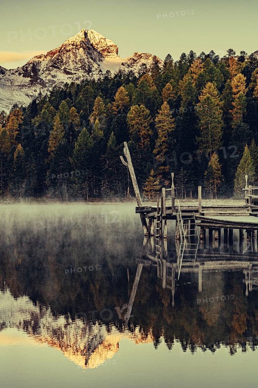 Lake Staz near Sankt Moritz in the Engadin in Switzerland. Morning atmosphere with fog in autumn. Water reflection and snow-covered mountains in the background