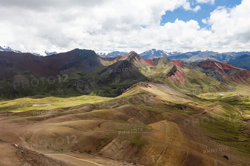 Panoramic view capturing the vibrant and varied hues of the mountainous terrain in the highlands of Peru, with distinct red and green mineral-rich hills under a cloudy sky