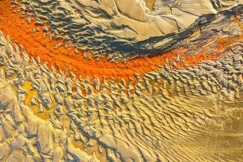Aerial capture of sand patterns showcasing vivid colors and intricate designs. The interplay of light and shadow highlights the textures and dynamic landscape features