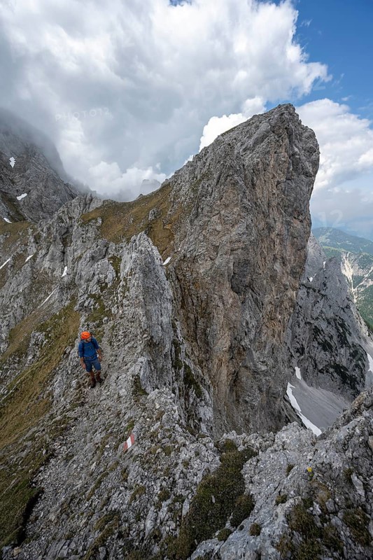 Mountaineer with helmet on a narrow hiking trail on a rocky ridge, ascent to the Maukspitze, clouds moving around the mountains, Ackerlpitze in the background, Wilder Kaiser, Kaiser Mountains, Tyrol, Austria